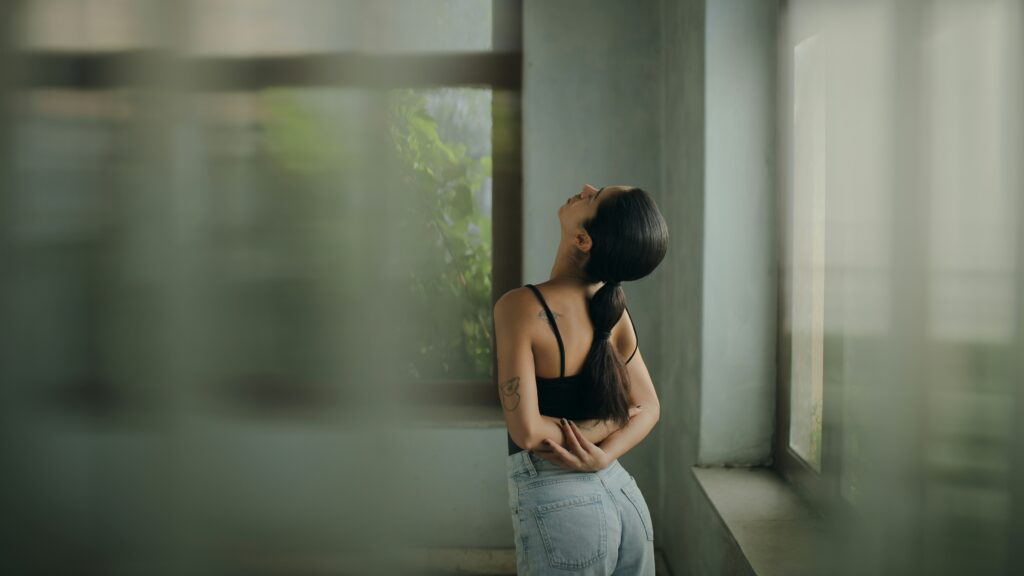 chronic pain therapy ontario woman standing in a hall facing away from camera with arms crossed behind her and head leaning back