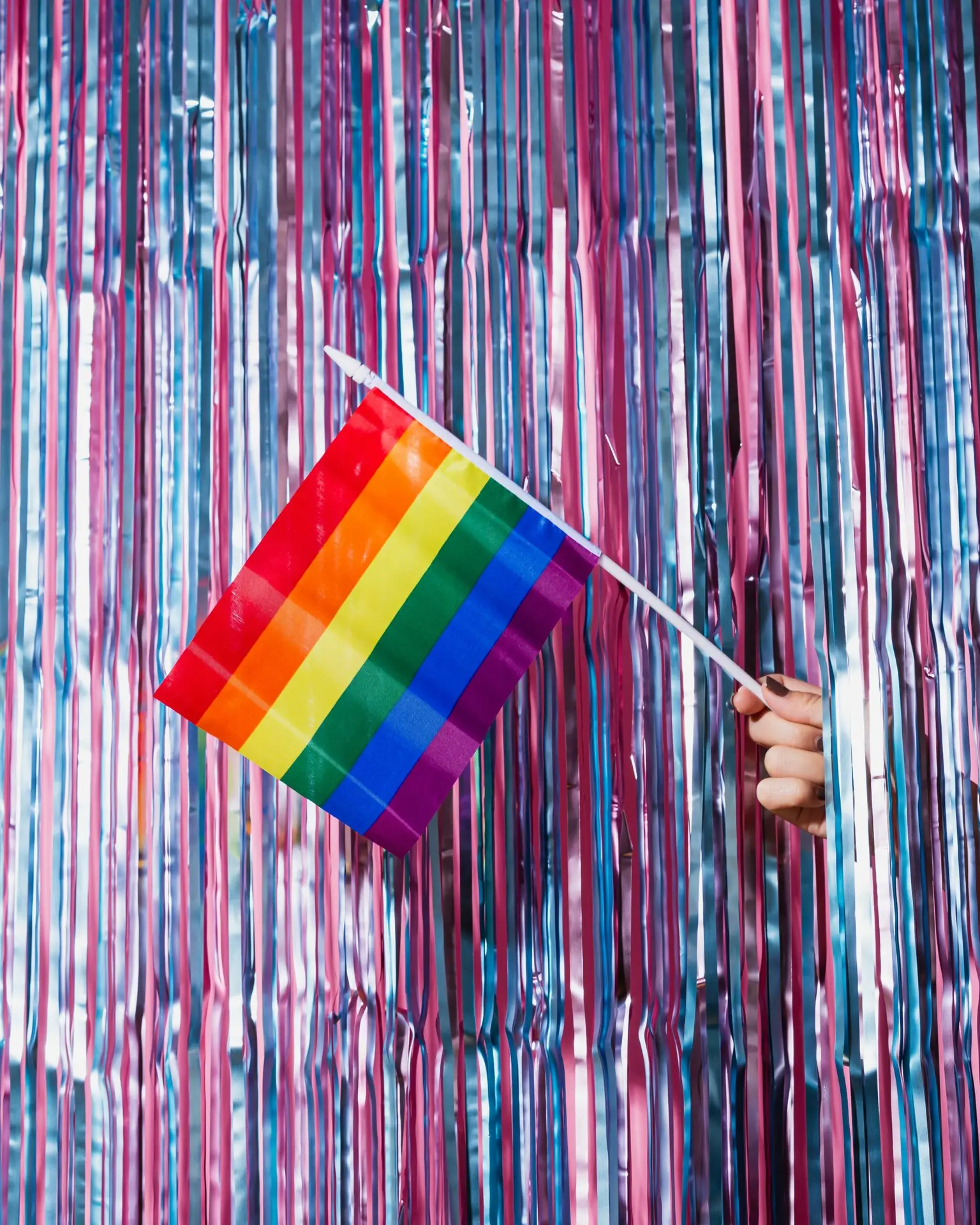 lgbtqia affirming therapy background of purple and blue tinsel with hand poking out holding a rainbow flag