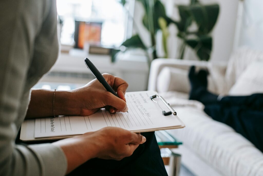 photo shows a woman (torso only) writing on a clipboard in front of a couch