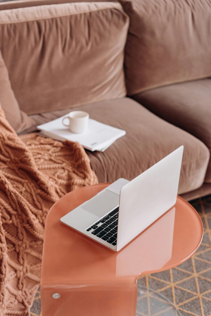 A blush couch with tan throw blanket over the arm, a notebook with a teacup on one cushion and a side table with an open laptop in front. virtual therapy ontario