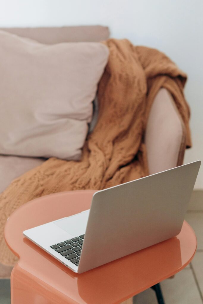 photo of a tan couch with brown blanket thrown over one arm and a side table with a laptop in front