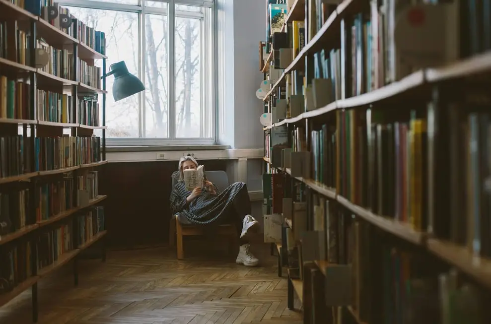 a woman on a chair at the end of an aisle of books reading