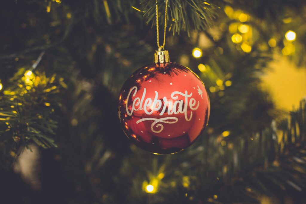 A close up of a red bauble on a christmas tree that says celebrate in calligraphy