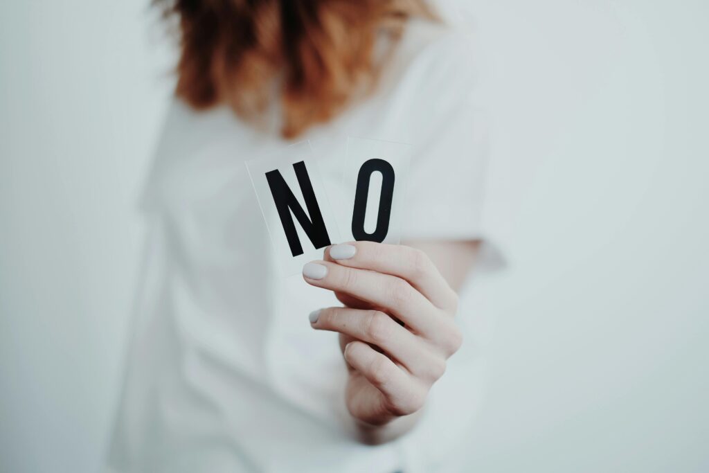 A person with red hair and a white t-shirt on is blurry in the background holding the word NO in her hand toward the camera