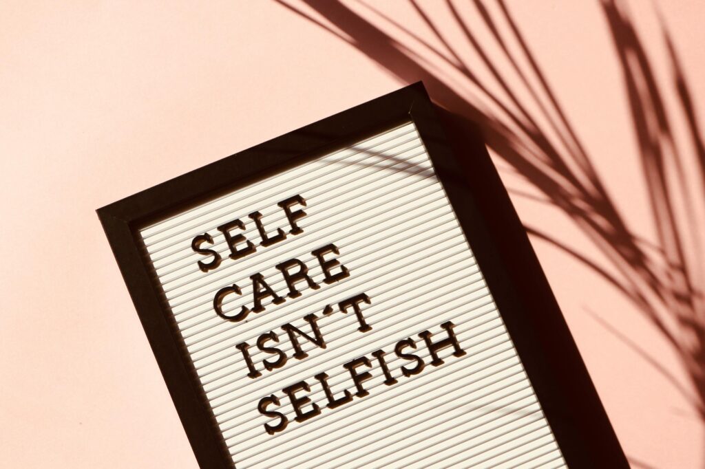 A message board with self care isn't selfish written on it against a pink wall.