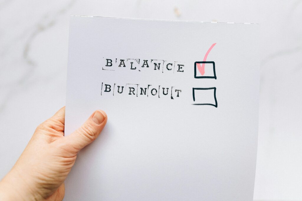 a hand is holding a sheet of paper with balance and burnout written on it with a check mark next to balance