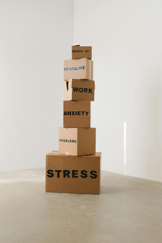 A stack of cardboard boxes with different words on them relating to stress such as work, anxiety, problems.