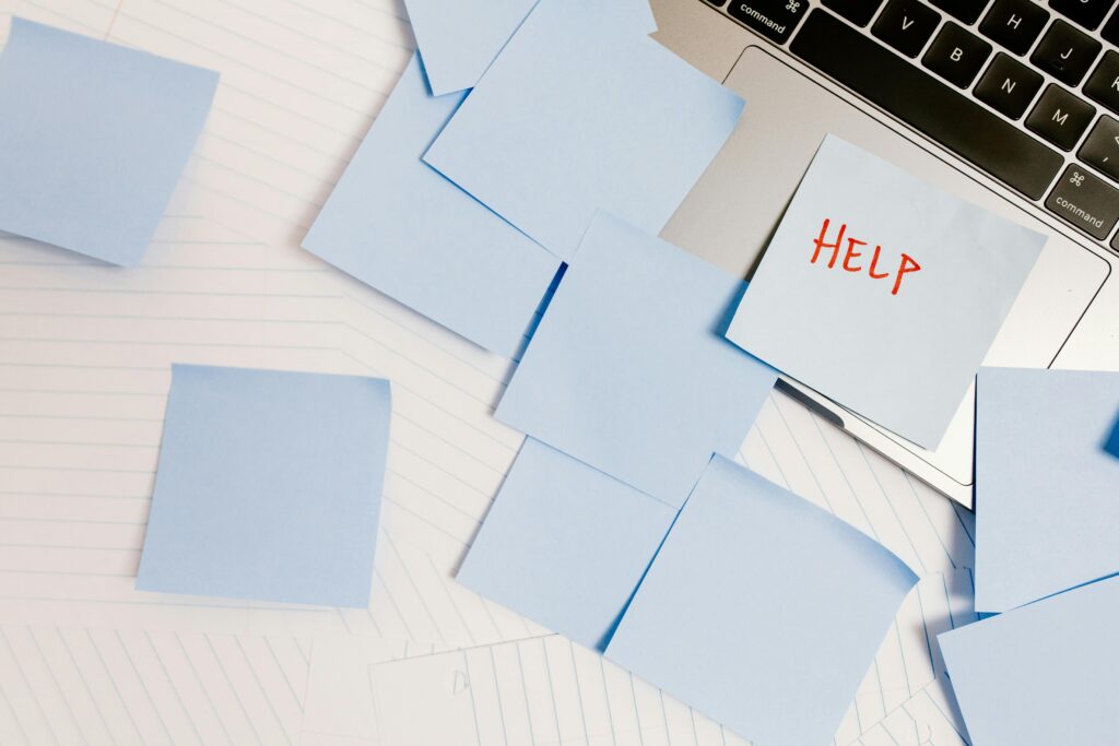 The corner of a laptop is seen with the table and laptop covered in blue sticky notes one of which says help in red.